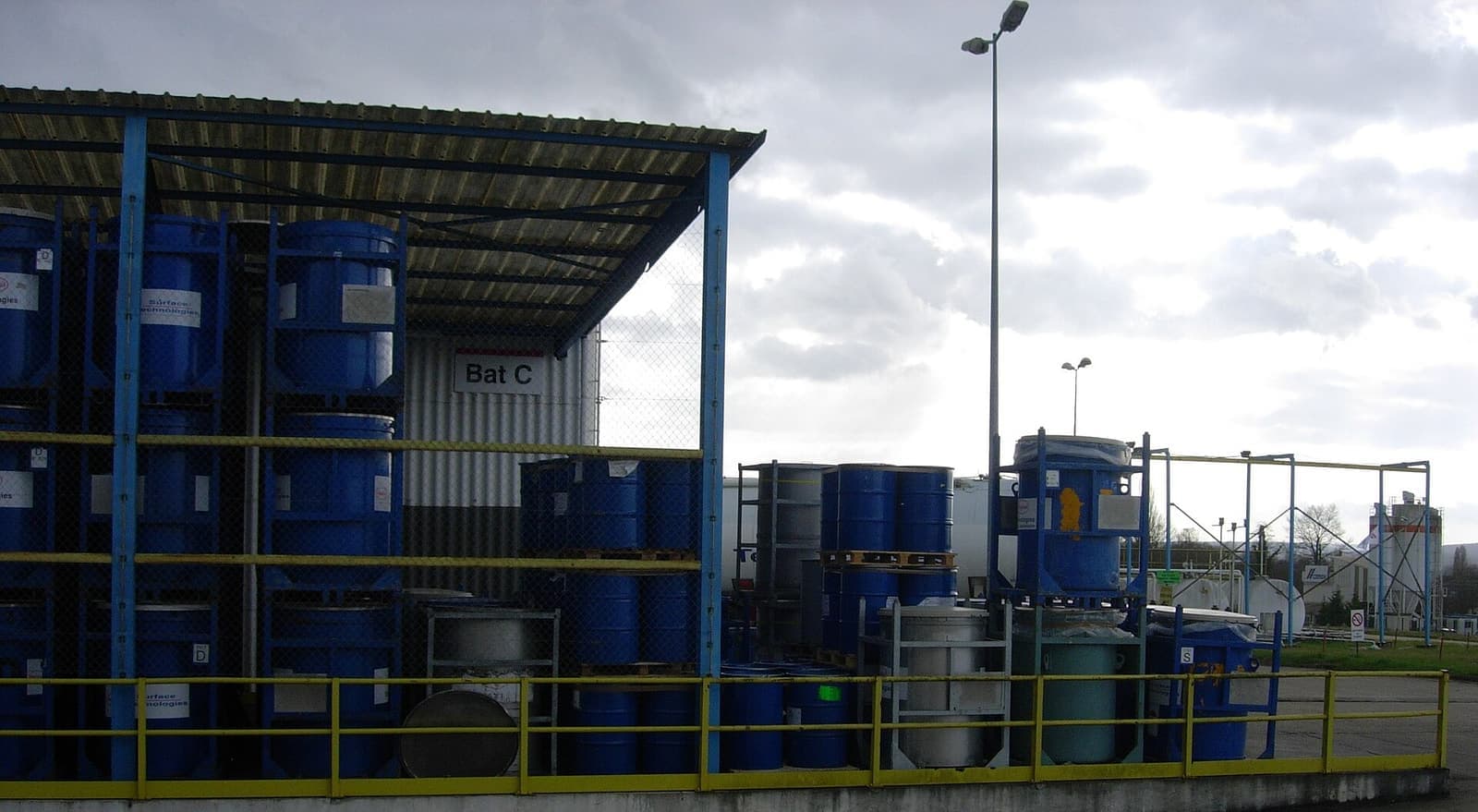 Tempat penyimpanan beratap berisi drum biru yang tertata di rak